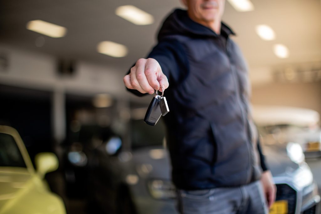 Een autosleutel wordt aangeboden, met de showroom op de achtergrond