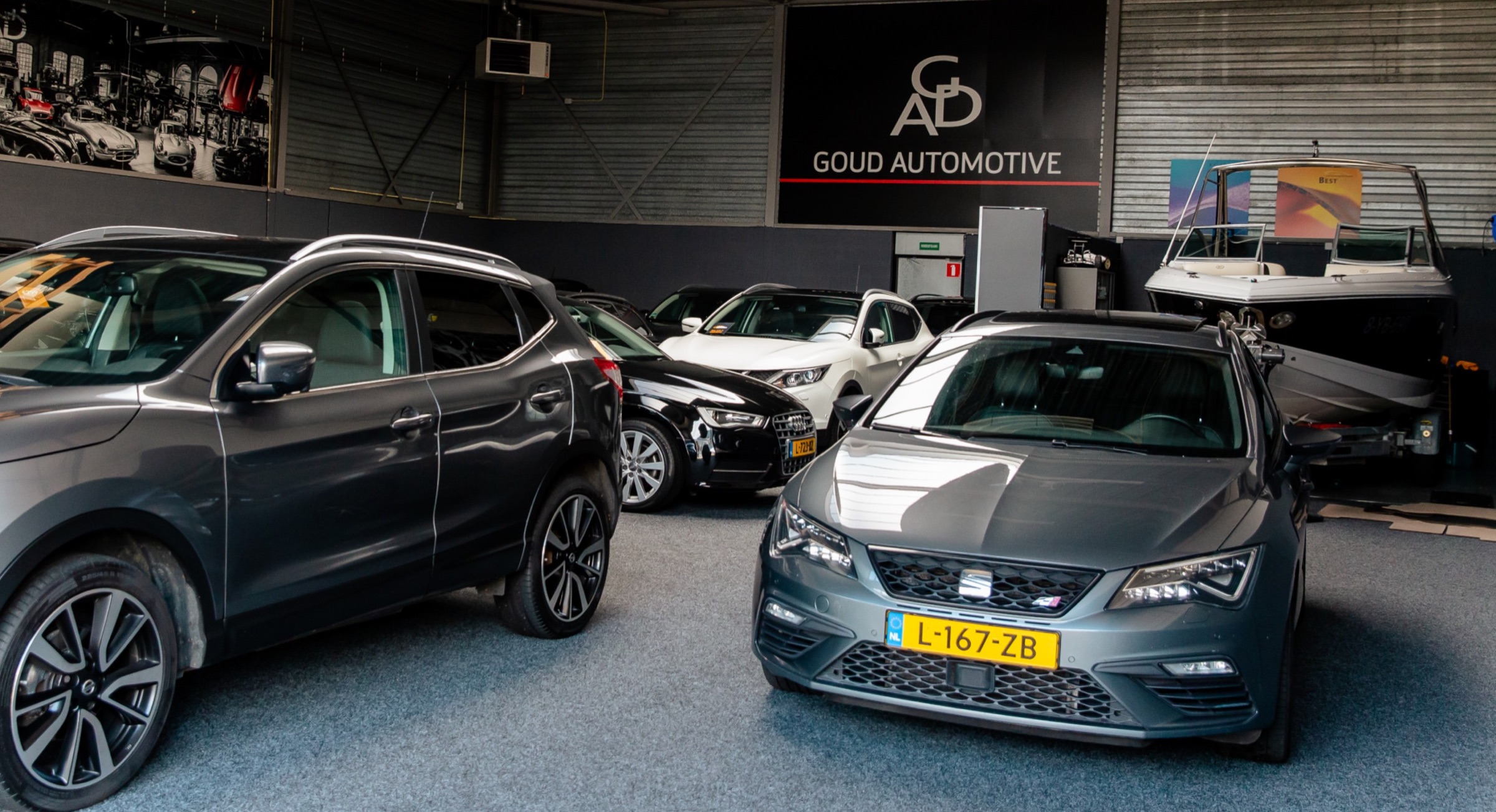 Auto's in de showroom van Goud Automotive, met het wandbord op de achtergrond
