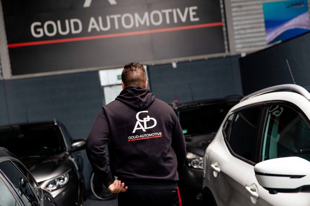 Een medewerker in een Goud Automotive-trui loopt tussen de auto's naar het wandbord